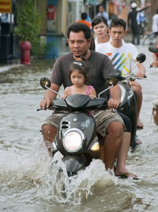 People ride motor scooters on a flooded street in a residential area of northern Bangkok