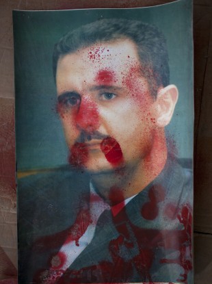 A portrait of Syrian President Bashar Al-Assad defaced with red paint is sown during an anti-government demonstration in the outskirts of Idlib in the north of the country