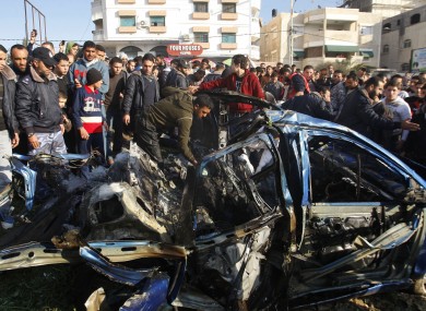 Palestinians gather around the wreckage of a car targeted in the airstrike that killed Zuhair al-Qaissi