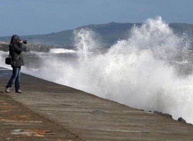 A woman photographs waves as they crash against the sea wall at Howth Pier in Dublin on Wednesday