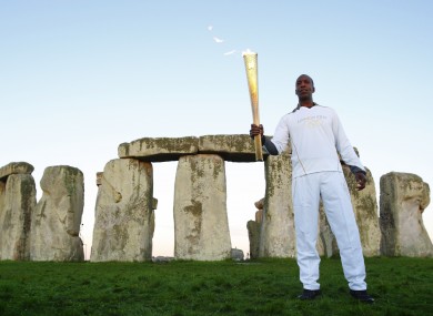 American 200 and 400 metre runner Michael Johnson holds the Olympic Torch at Stonehenge.