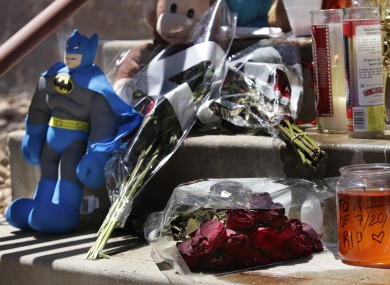 Candles, flowers, and a Batman figure are shown at a memorial.
