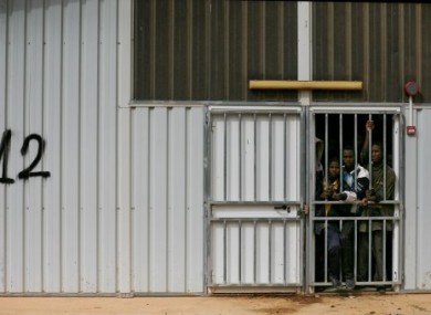 illegal African immigrants and suspected mercenaries stand at a barred door in a prison in Gherian, Libya last February