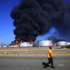 A man walks past the still-burning Amuay refinery on Sunday. (AP Photo/Ariana Cubillos/PA)