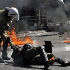 A riot policeman assists a colleague after he was hit by a petrol bomb thrown by protester. (AP Photo/Nikolas Giakoumidis)